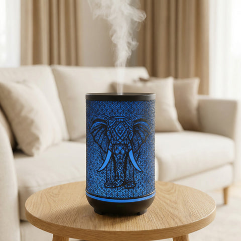 Black metal diffuser with blue LED elephant silhouette pattern misting on wood table in living room, Aroma Paradise