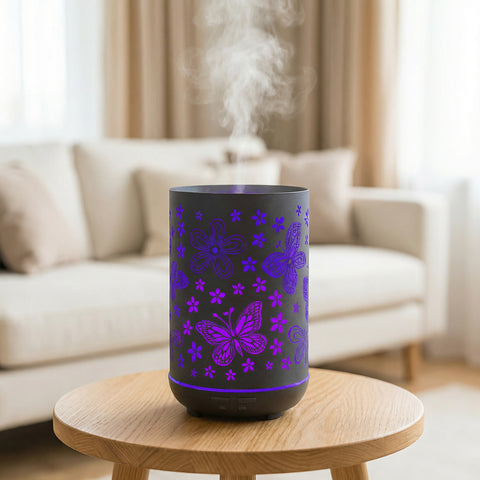 Black metal diffuser with purple LED butterfly and flower cutout patterns misting on wood table, Aroma Paradise