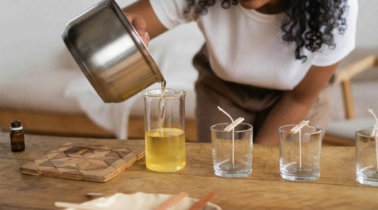 Person pouring melted wax with fragrance oil into glass jars for candle making