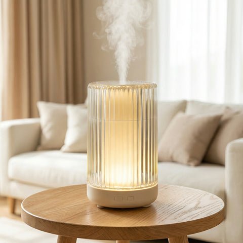 Clear ribbed cylindrical diffuser with warm amber LED glow misting on side table - Aroma Paradise