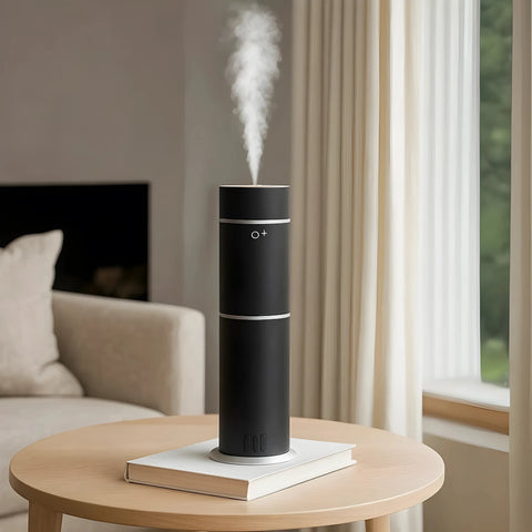 Black humidifier on a table with steam rising, in a living room setting.