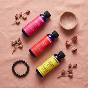 Floral oil set flat lay on pink linen with dried rosebuds and black lava bead bracelet, Aroma Paradise