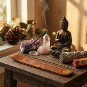 Smoking incense in wooden holder with Buddha statue, crystals, and sage on sunlit table - Aroma Paradise