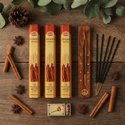 Hem Cinnamon incense flat lay with three tubes, wooden holder, cinnamon sticks, and star anise on wood - Aroma Paradise
