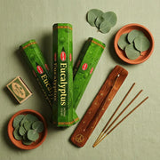 Hem Eucalyptus gift set flat lay with three green boxes, wooden holder, eucalyptus leaves, and terra cotta bowls - Aroma Paradise