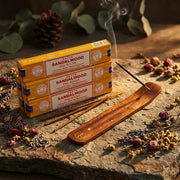 Three yellow Satya Sandalwood boxes with smoking stick in wooden holder on stone with dried flowers - Aroma Paradise