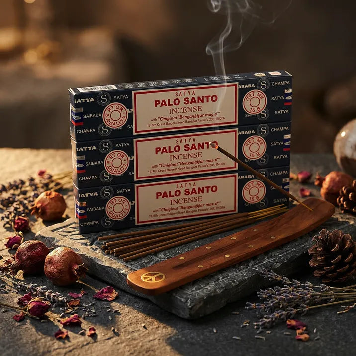 Three Satya Palo Santo blue boxes with smoking stick in wooden holder on dark stone with dried botanicals - Aroma Paradise