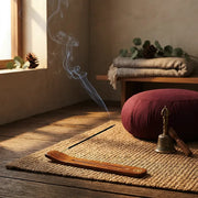 Smoking incense in wooden holder on jute mat with meditation cushion and brass bell in sunlit zen room - Aroma Paradise