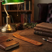 Smoking incense in wooden holder on study desk with green banker lamp, leather journal, and books - Aroma Paradise