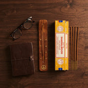 Satya Sandalwood gift set flat lay with yellow box, wooden holder, sticks, leather journal, and glasses - Aroma Paradise