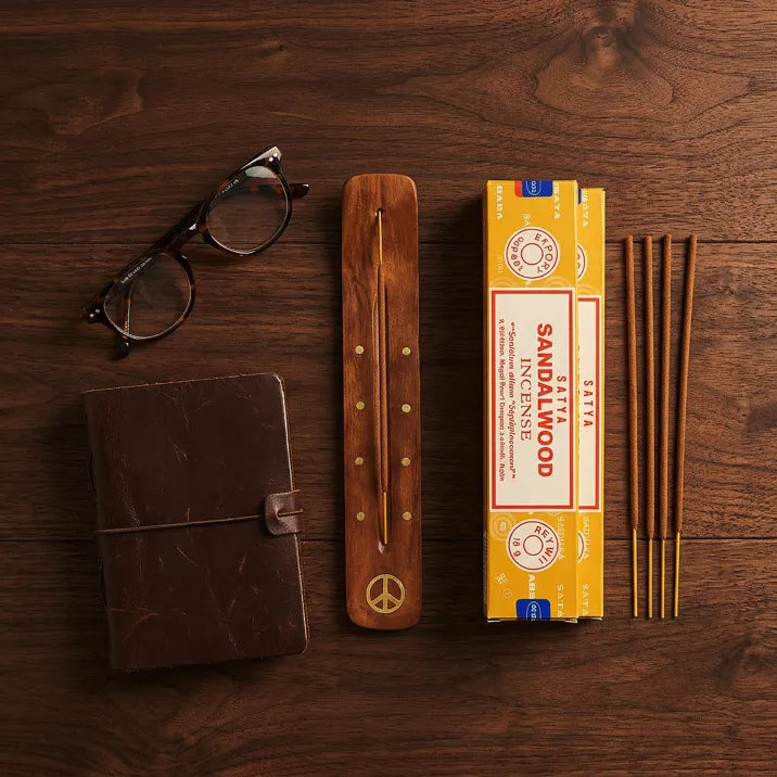 Satya Sandalwood gift set flat lay with yellow box, wooden holder, sticks, leather journal, and glasses - Aroma Paradise