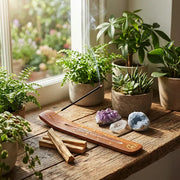 Satya Palo Santo incense stick burning on wooden holder with crystals and plants by a window - Aroma Paradise