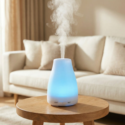 White vase-shaped LED diffuser glowing blue with cool mist on a side table in living room - Aroma Paradise