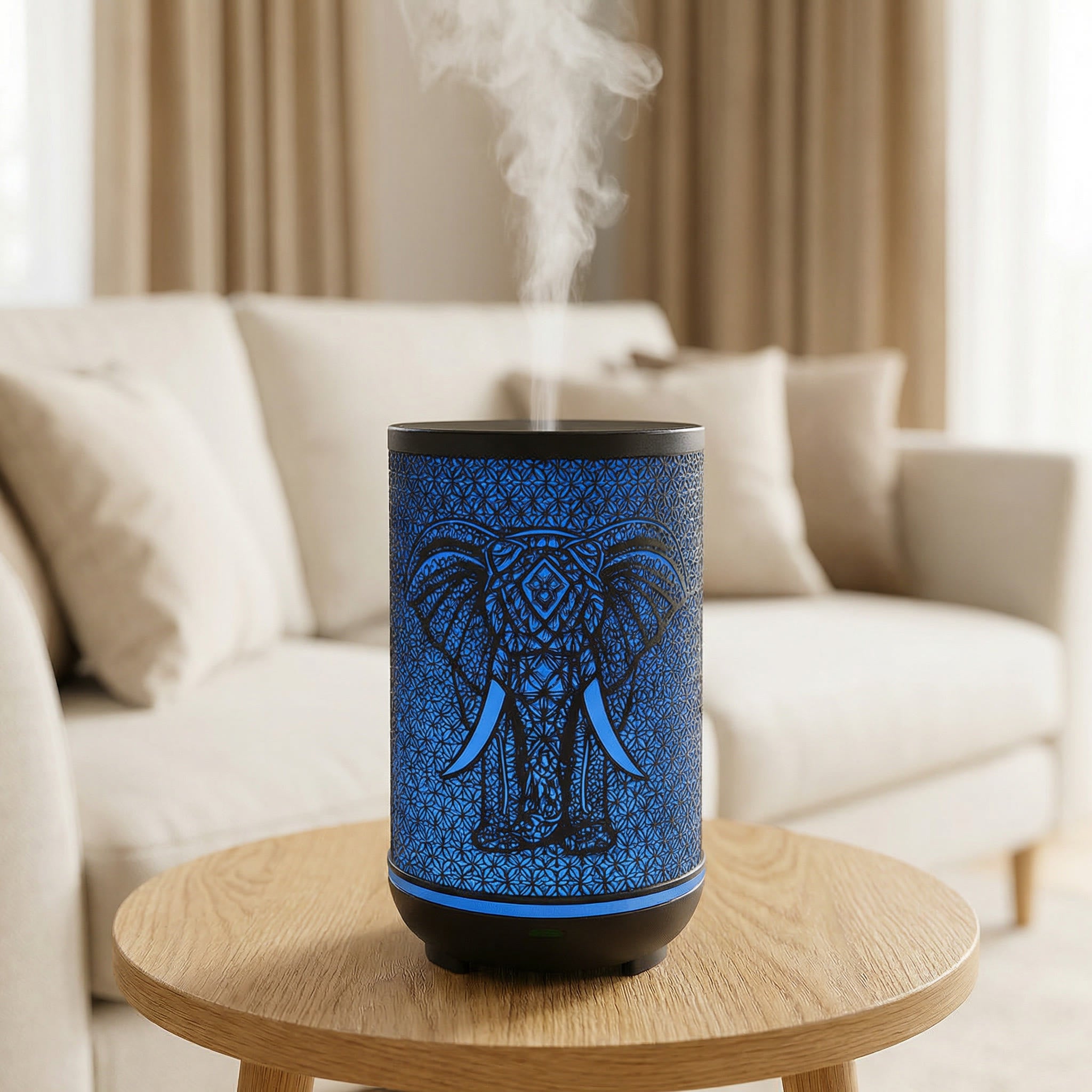 Black metal diffuser with blue LED elephant silhouette pattern misting on wood table in living room, Aroma Paradise