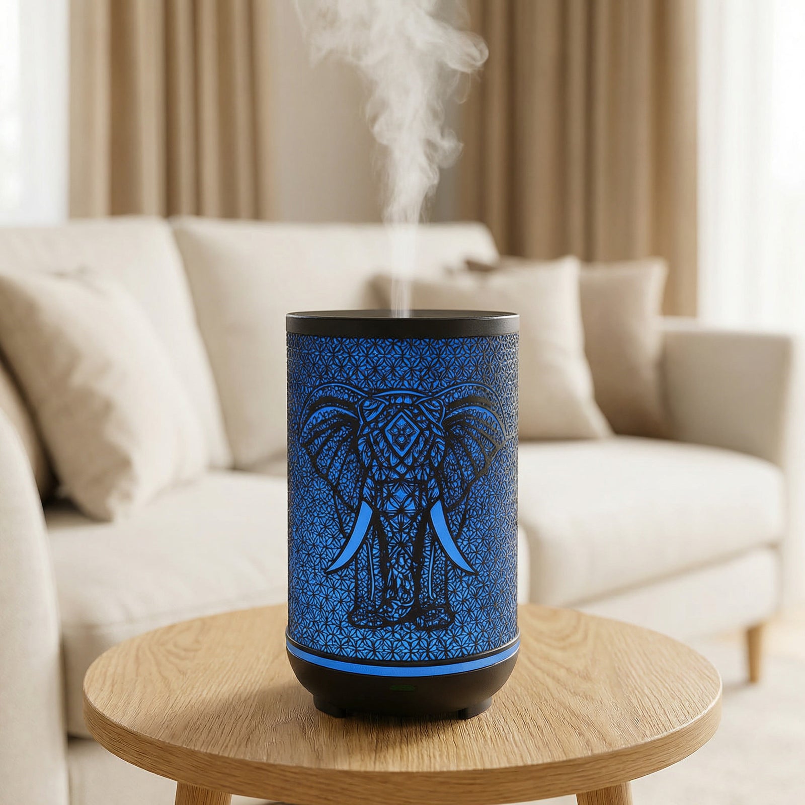 Black metal diffuser with blue LED elephant silhouette pattern misting on wood table in living room, Aroma Paradise